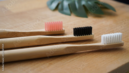 Pink  black and white color of eco-friendly bamboo toothbrushes with blurred leaf on a wood background. Natural organic dental concept