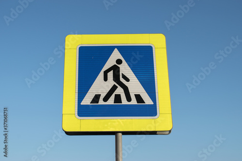 square road sign of a pedestrian crossing with reflective elements on a blue sky background