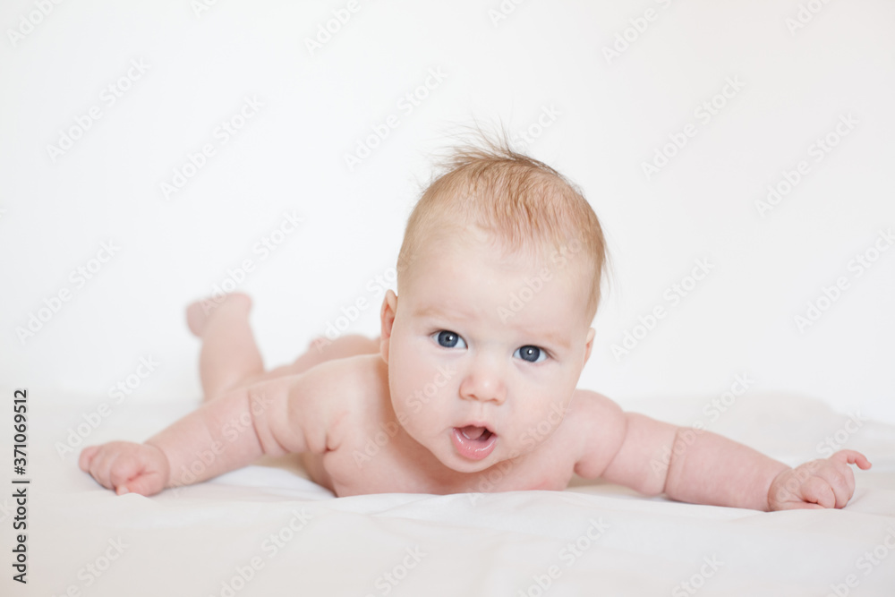 small child, baby lies on his stomach and smiles. On a white background. Newborn baby. three months old baby. A baby of European appearance. selective focus small child, baby lies on his stomach and smiles. On a white background. Newborn baby. three months old baby. A baby of European appearance. selective focus