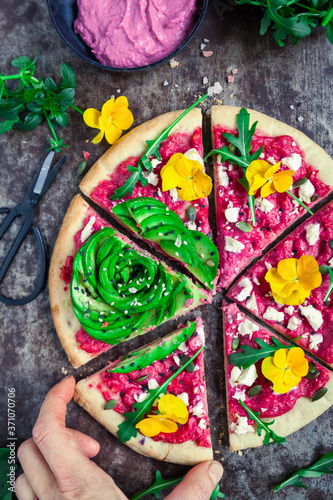 Healthy beetroot hummus pizza with an avocado rose and edible flowers, old baking tray background
