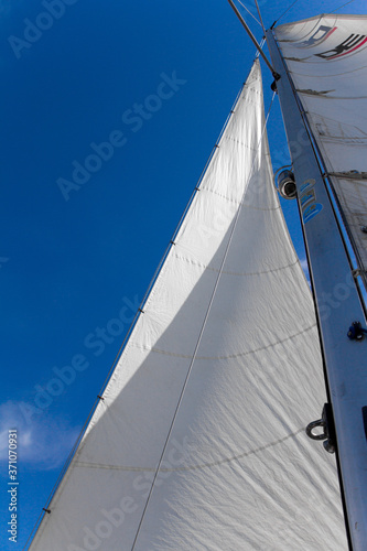 Bottom view of mast and sail of yacht on blue sky background, selective focus