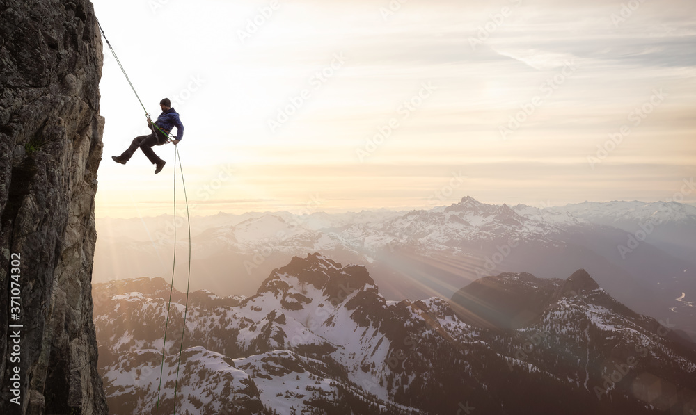 Epic Adventurous Extreme Sport Composite of Rock Climbing Man Rappelling  from a Cliff. Mountain Landscape Background from British Columbia, Canada.  Concept: Explore, Hike, Adventure, Lifestyle Stock Photo