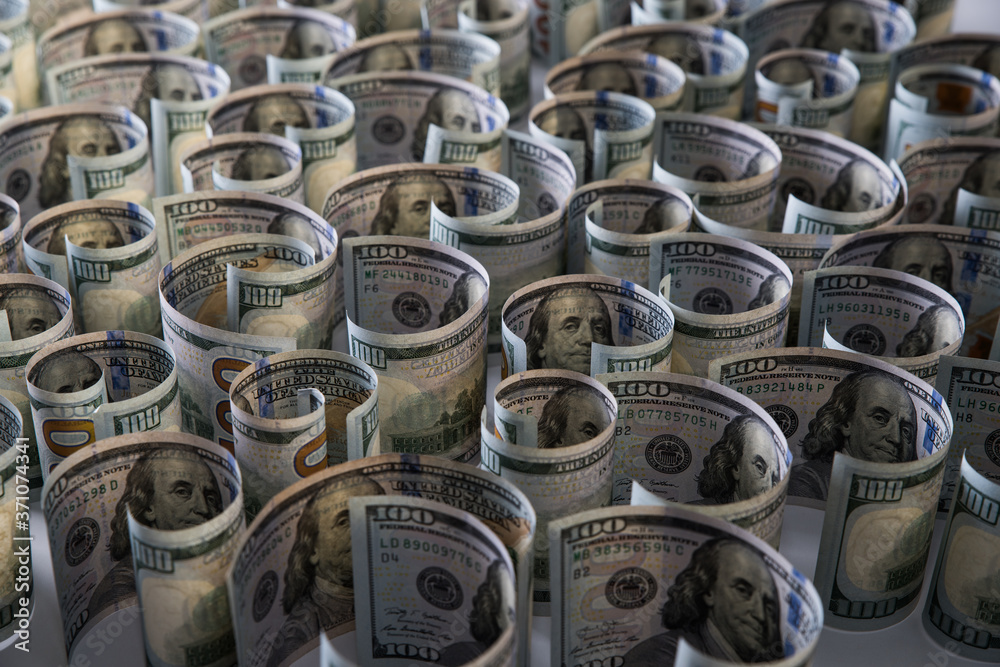Lots of hundred dollar bills close-up rolled up on a white background. Selective focus. Blurred background. Lots of hundred dollar bills close-up rolled up on a white background. Selective focus. Blurred background.