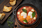 hearty English breakfast - poached eggs, with tomatoes and sauce in a pan on a wooden board
