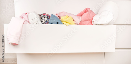 Оpen chest drawers with drop-down clothes and piles of clothes around in a mess