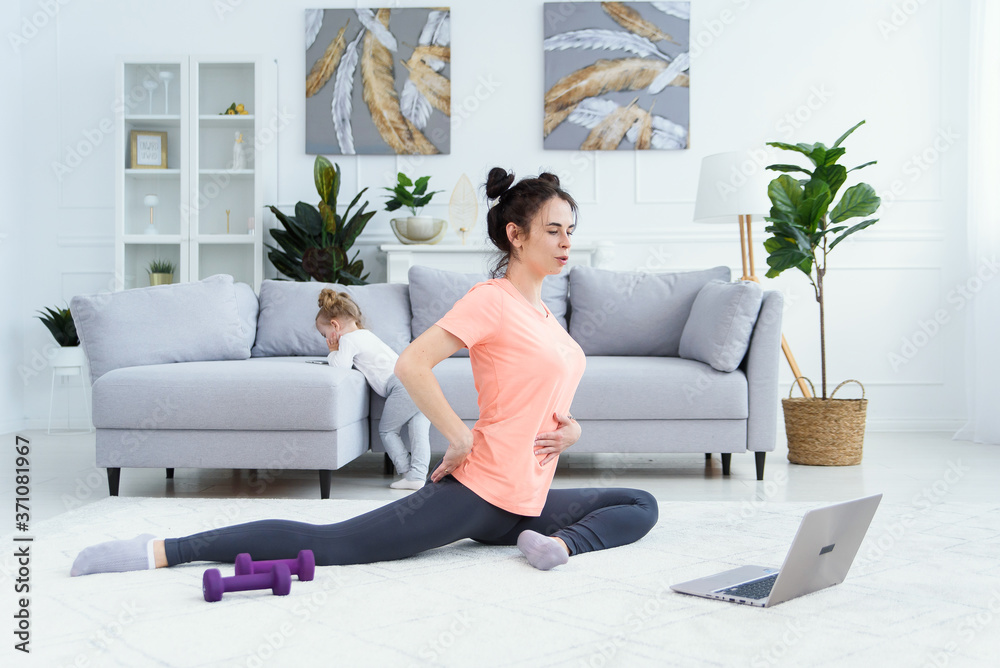 Fitness woman exercising on the floor at home and watching fitness videos in a laptop. Pretty girl doing online fitness workout. Fitness woman exercising on the floor at home and watching fitness videos in a laptop. Pretty girl doing online fitness workout.