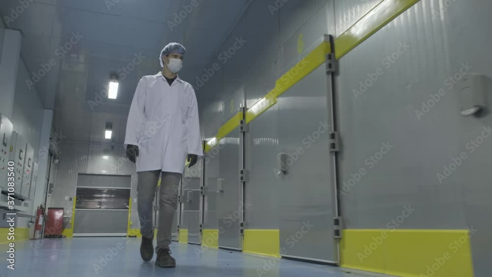 Worker in white workwear and mask walks along workshop. food engineer checks machines. worker or engineer walking through the workplace Worker in white workwear and mask walks along workshop. food engineer checks machines. worker or engineer walking through the workplace