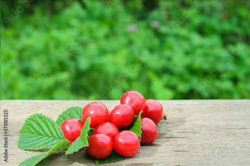 Red, ripe cherry berries with a twig and leaves on a rough woode