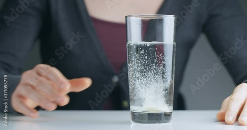 A woman drops an effervescent tablet in a glass of water and waits as it dissolves.