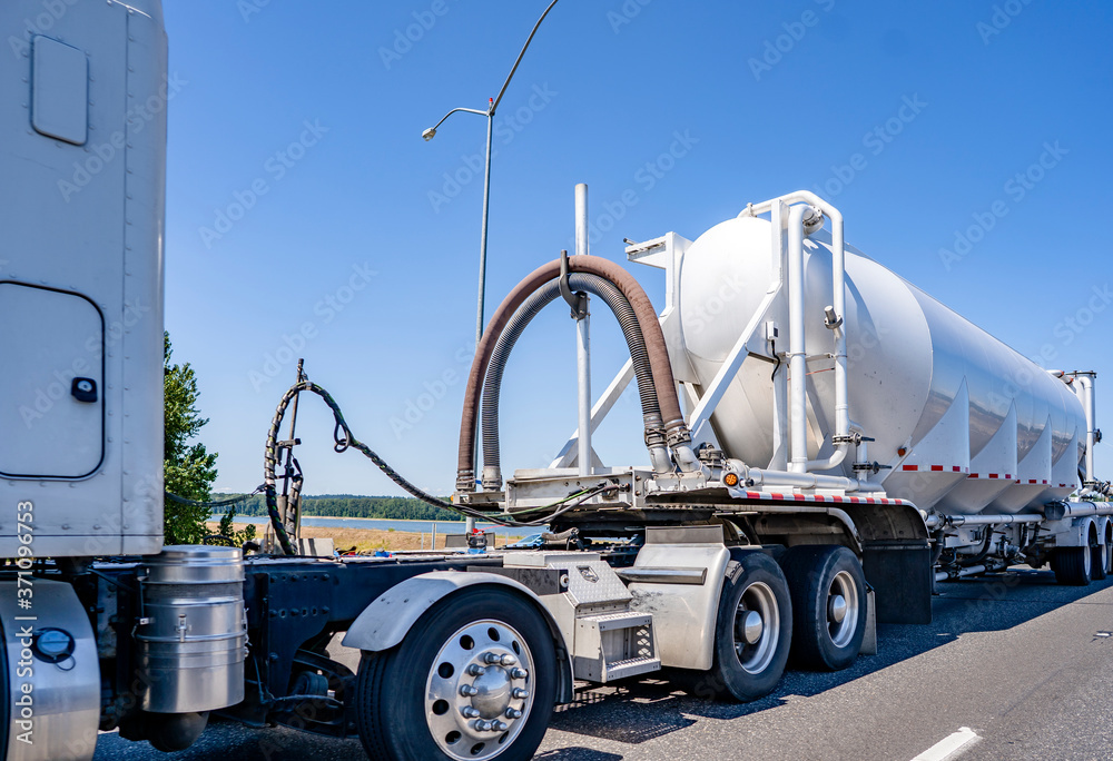 Big rig powerful semi truck transporting commercial cargo in specially equipped tank semi trailer running on the highway road