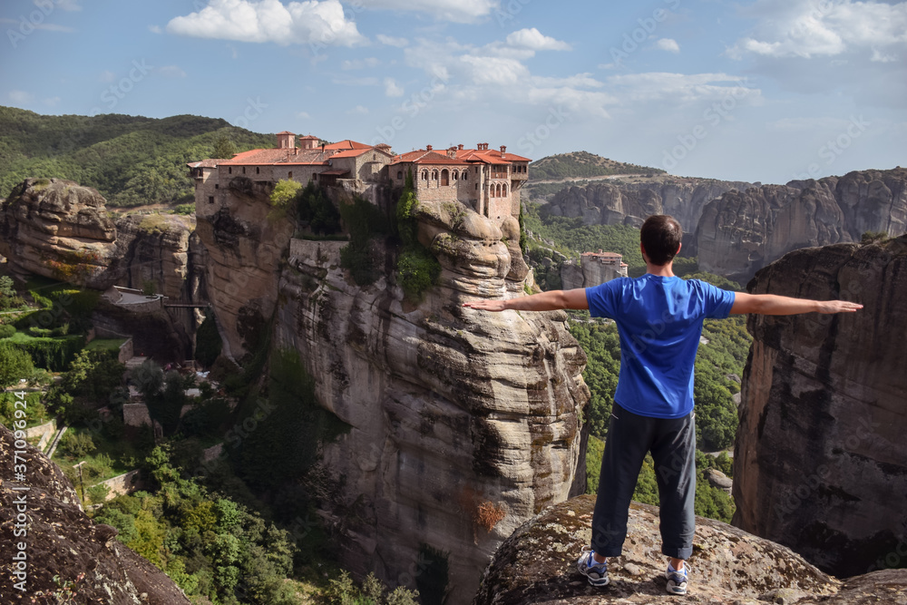 Western man opening arms facing dramatic landscape of Meteora monasteries built on vertical rock formations in Greece