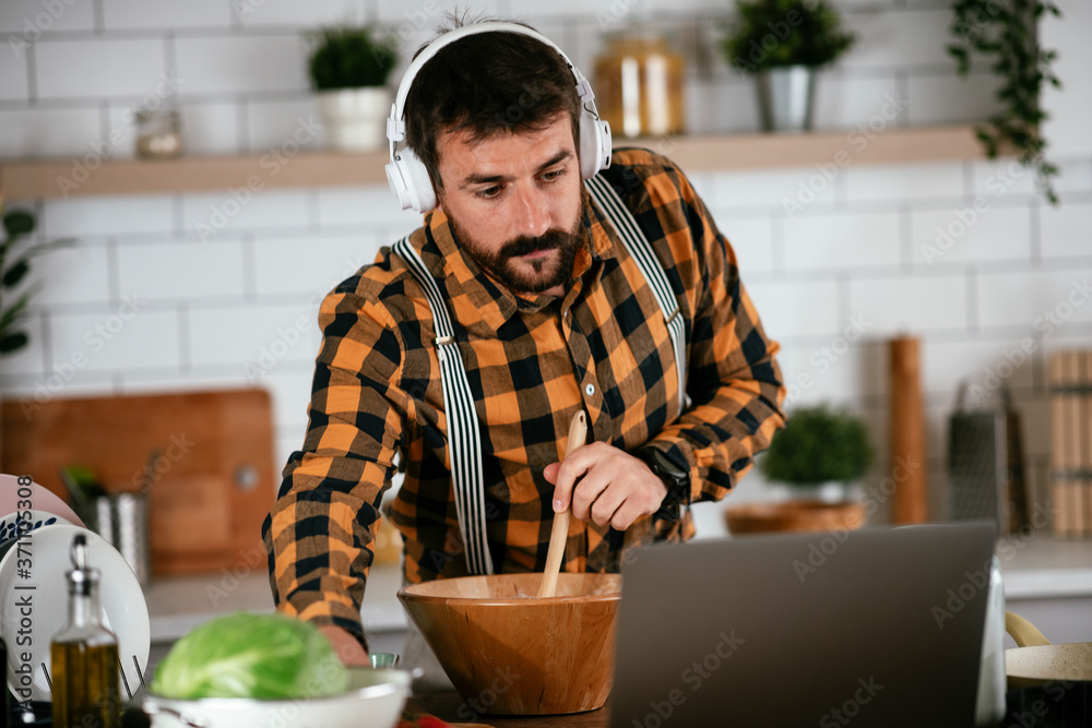 Portrait of handsome man in kitchen. Young man cooking while having video call.. Portrait of handsome man in kitchen. Young man cooking while having video call..