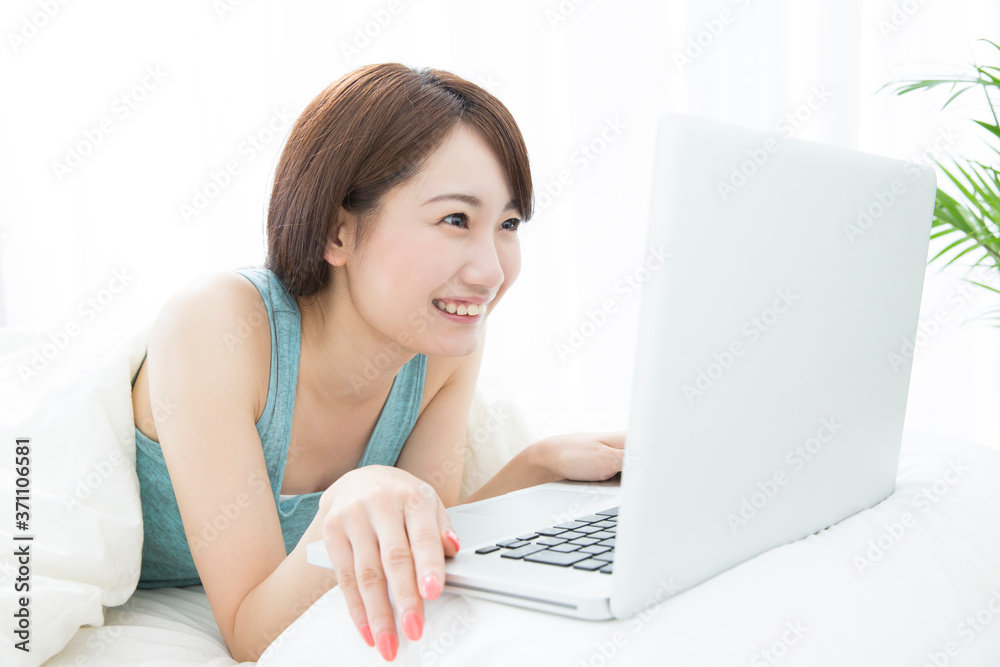 ベッドで寝転びながらノートパソコンを見る女性 ベッドで寝転びながらノートパソコンを見る女性