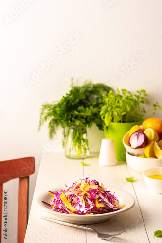 Light summer salad of red cabbage, onions and yellow bell peppers, salad in a plate on a white wooden table, olive oil with spices for dressing and basil with dill