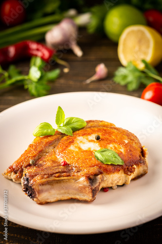 Fried pork entrecote on the bone, cooked pieces of pork meat with basil leaves and spices, steak on the bone in a plate on a wooden background