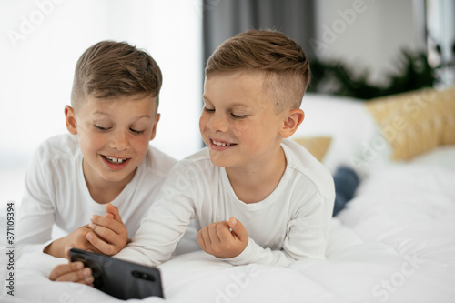 Two little brothers are playing games on the phone. Beautiful boys enjoying at home... © JustLife