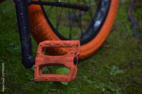 wet bike, with orange pedals and tires, on grass and moss