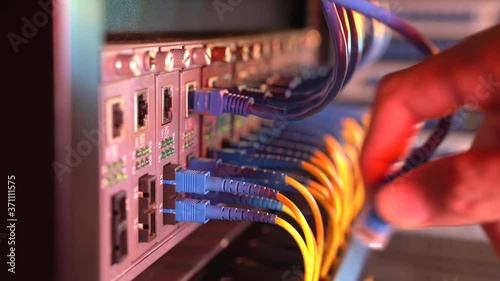 man working in network server room with fiber optic hub for digital communications and internet.