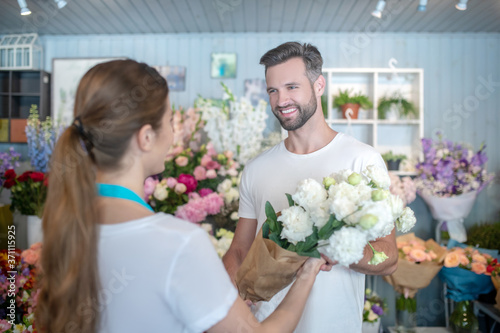 Smiling male taking bouquet of white flowers from female florist