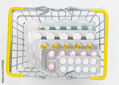 Various Pills in blisters are in a small shopping basket on a white background. Sale of drugs in stores and pharmacies. Health and medicine.