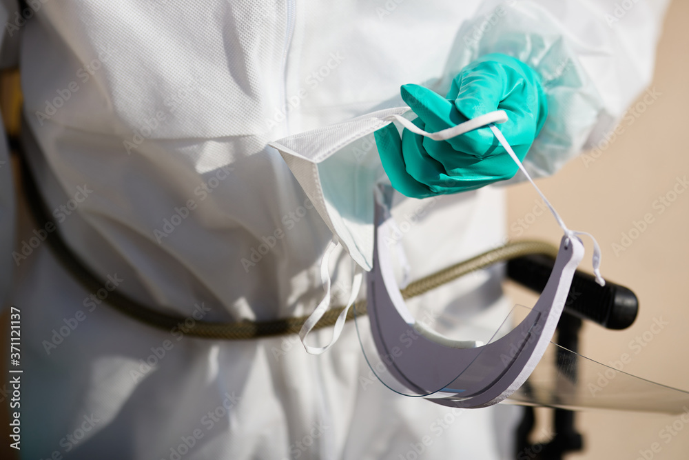 Close-up of man in hazmat suit holding visor and protective face mask. Close-up of man in hazmat suit holding visor and protective face mask.