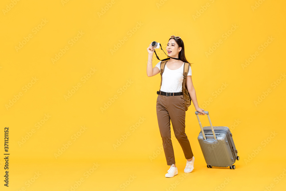 Full length travel portrait of excited young tourist Asian woman walking while taking photo with camera in isolated studio yellow background Full length travel portrait of excited young tourist Asian woman walking while taking photo with camera in isolated studio yellow background