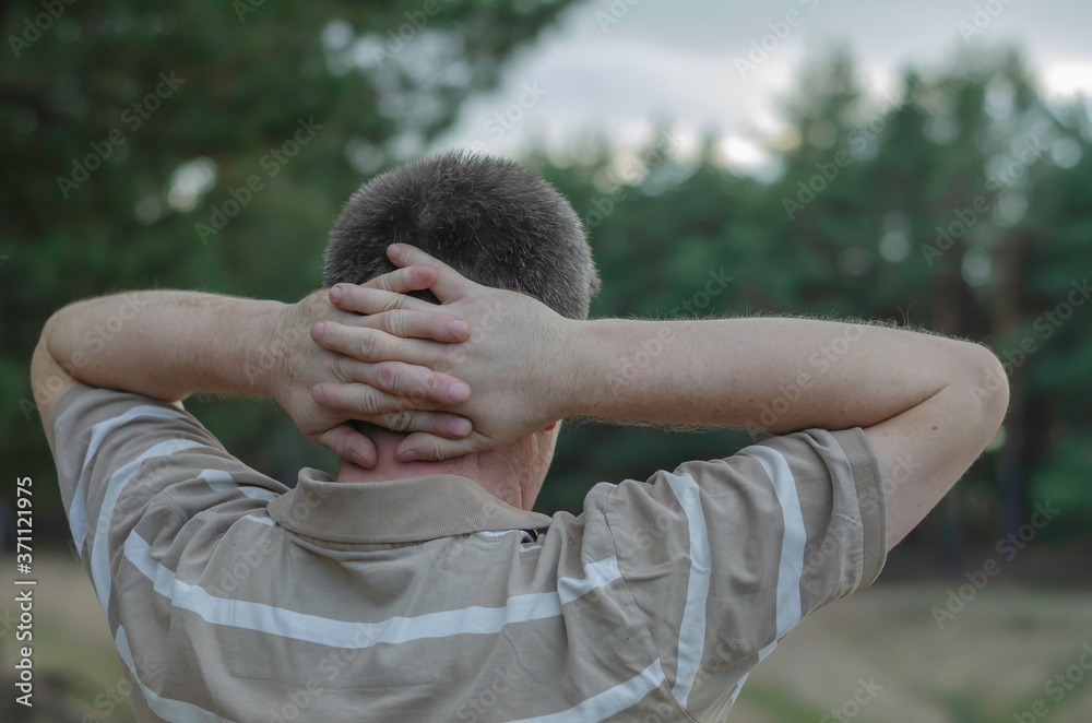 A view from the back of a mature man with fingers crossed behind his head. A view from the back of a mature man with fingers crossed behind his head.