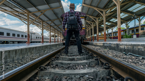 A young man standing on a train track at Chiang Mai Railway Station, Thailand with a back view.