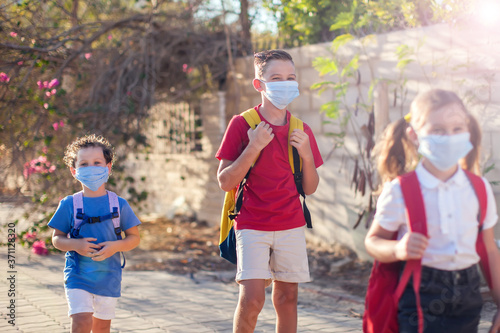 Pupils with medical masks on face and backpacks going to school. Education during coronavirus time. Back to school.