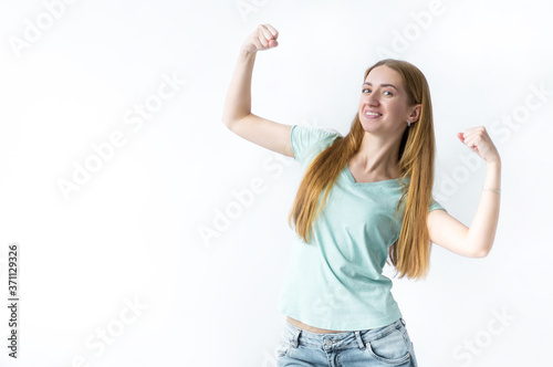 The girl raises her arms to show that her muscles are confident of victory, look strong and independent, smiles positively at the camera, stands on a white background. Sports concept.