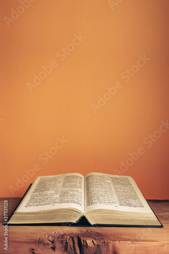Open Holy Bible on a old wooden table. Beautiful orange wall background..