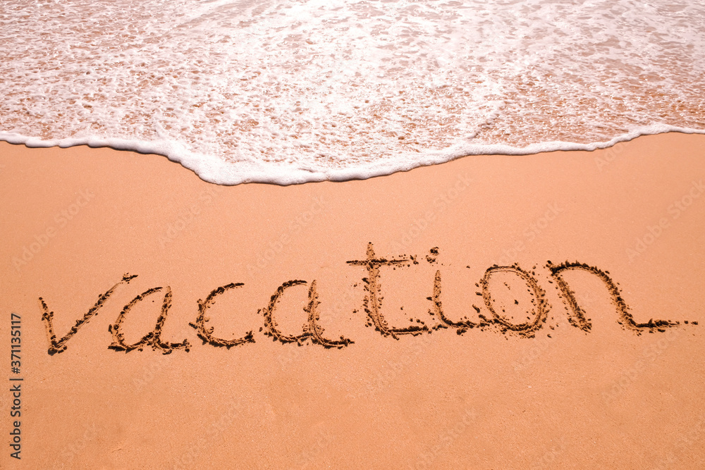 Fototapeta premium Word Vacation hand written in the sand with a sea wave. Close up sand texture on beach in summer.