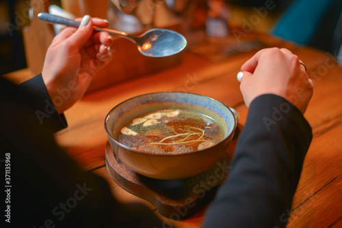 Young woman eating soup served in a white bowl. Eating out. Restaurant concept. Woman' s hand holding spoon.