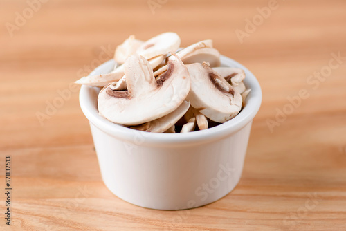 Sliced champignon mushrooms in a bowl isolated on wooden background. Snack, appetizer. Pizza ingredient.