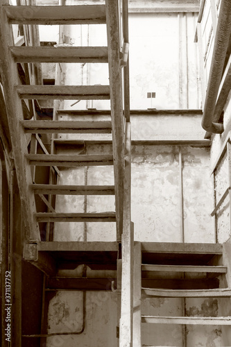 Rusty metal ladder up abandoned building. The crisis, the fall of the economy, to stop production capacity led to the collapse. Global catastrophe. Old photo effect