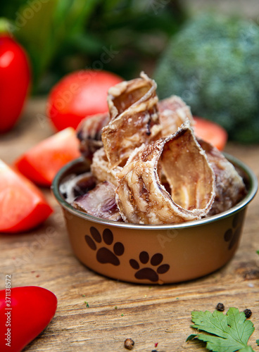 Dried beef tracheas in the dog vessel  on the wooden board and some vegetables on the background. Chewing treats for domestic dogs. Natural dental treats for promotion and pampering.
