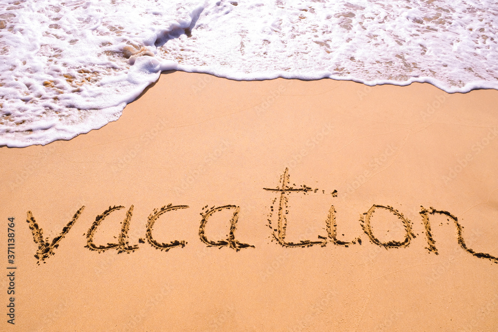 Fototapeta premium Word Vacation hand written in the sand with a sea wave. Close up sand texture on beach in summer.