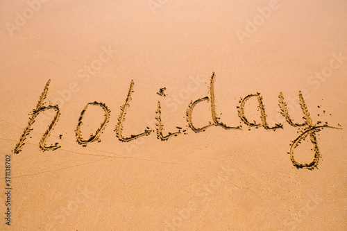 Word Holiday hand written in the wet sand. Close up sand texture on beach in summer.