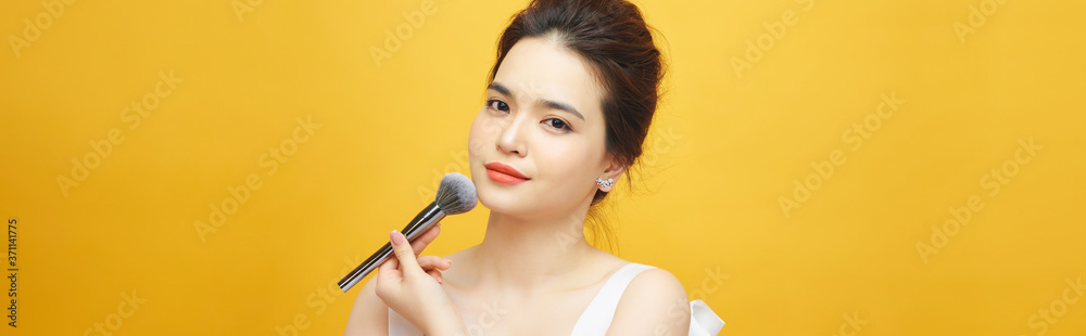 beautiful woman holding makeup brush over yellow beautiful woman holding makeup brush over yellow