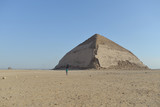 a tourist walks alone through the desert in front of The Bent Pyramid an ancient Egyptian pyramid located at the royal necropolis of Dahshur