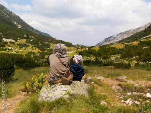 Man and little boy in mountains sit on rock and look into distance