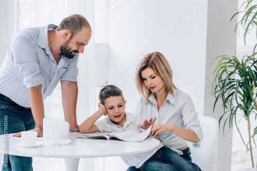 The family sits in a room on the white floor and dabbles in hugging laughs. mother  father and teenage son are hugging on the floor