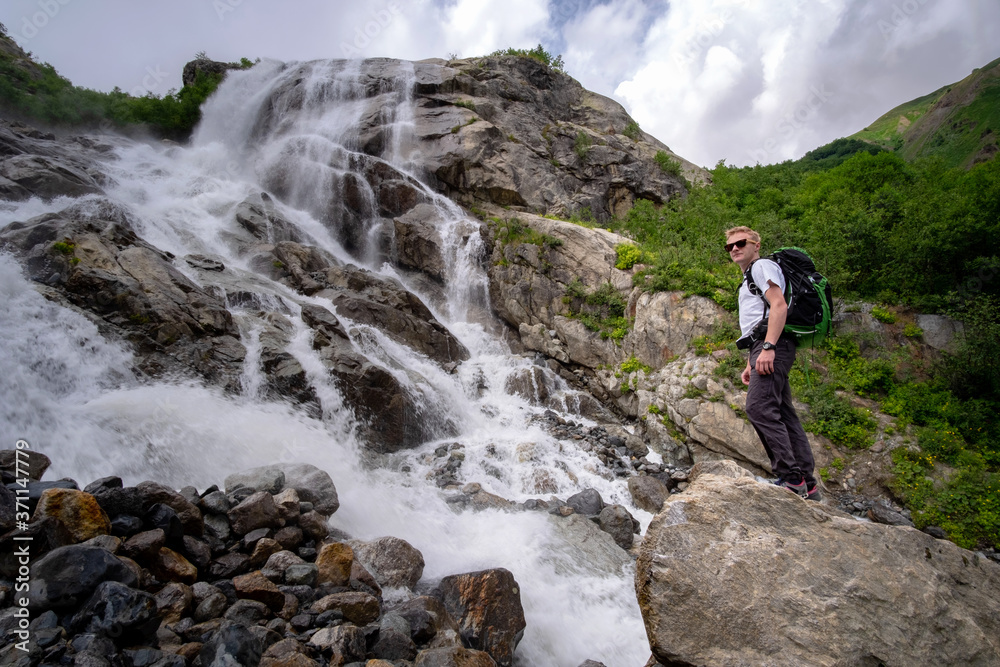 Man hiking with backpack looking at waterfall. Portrait of male adult back standing outdoor.