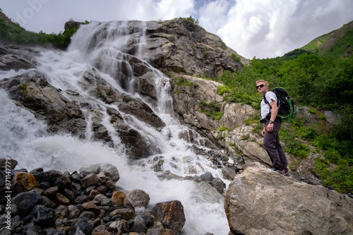 Man hiking with backpack looking at waterfall. Portrait of male adult back standing outdoor.