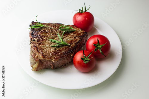 grilled steak with vegetables on a white plate, seasoned with pepper and rosemary, close-up
