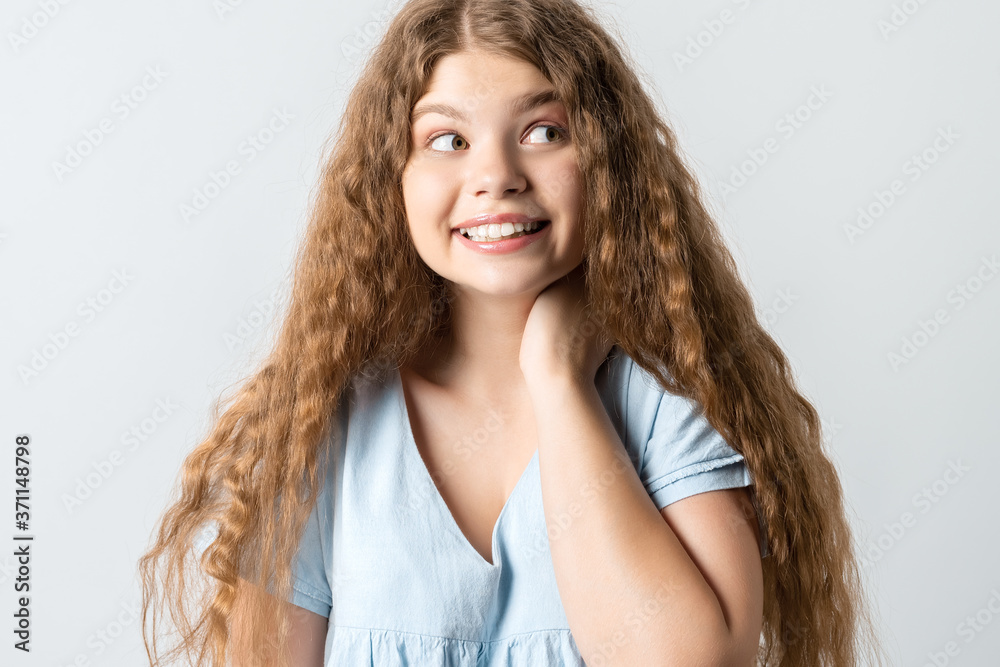 Attractive Positive young woman with curly long hairstyle has tender smile, keeps hand on neck Attractive Positive young woman with curly long hairstyle has tender smile, keeps hand on neck