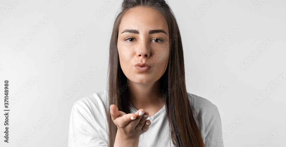 Beautiful young woman with long chestnut hair makes air kiss, blows over palm Beautiful young woman with long chestnut hair makes air kiss, blows over palm