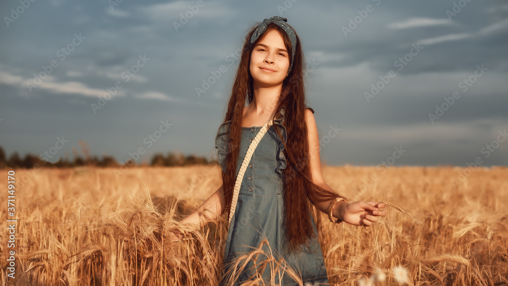 Obraz premium Portrait of Little girl 10-12 years old with long brown hair, walk in a wheat field on a summer evening