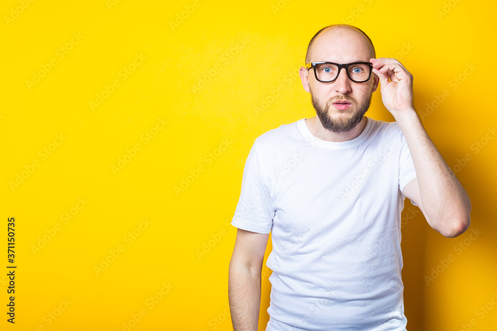 Serious bearded bald young guy with glasses on yellow background.