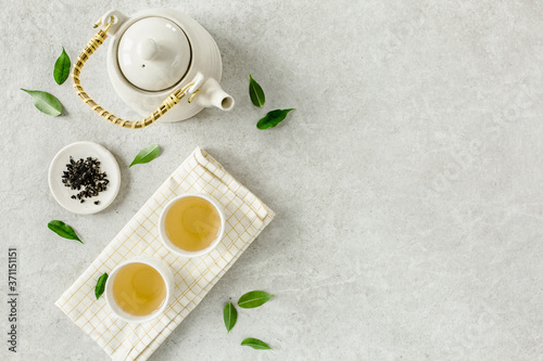 Herbal tea with two white tea cups and teapot, with green tea leaves. Flat lay, top view. Tea concept